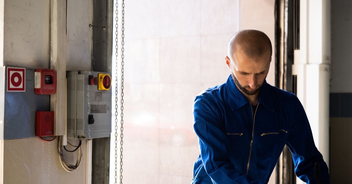 Técnico de manutenção junto a quadro elétrico em corredor de prédio