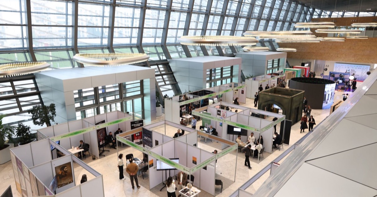 Vista ampla de pavilhão de feira com estandes e visitantes