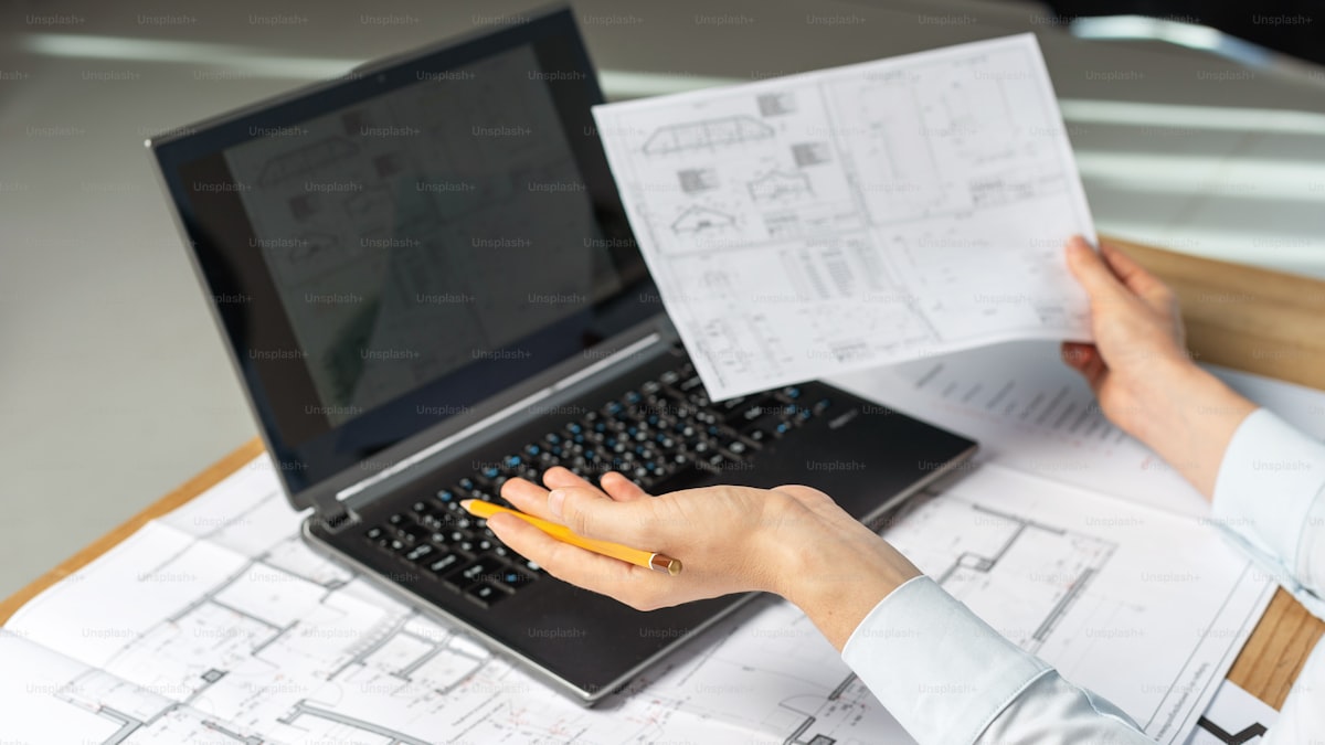 Profissional revisando plantas no laptop durante a negociação de um contrato de engenharia