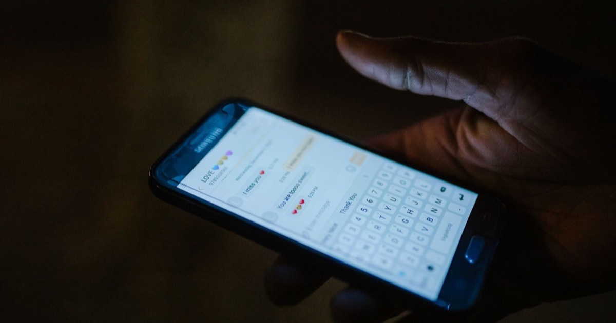 Mão segurando celular com conversa de aplicativo de mensagens aberta
